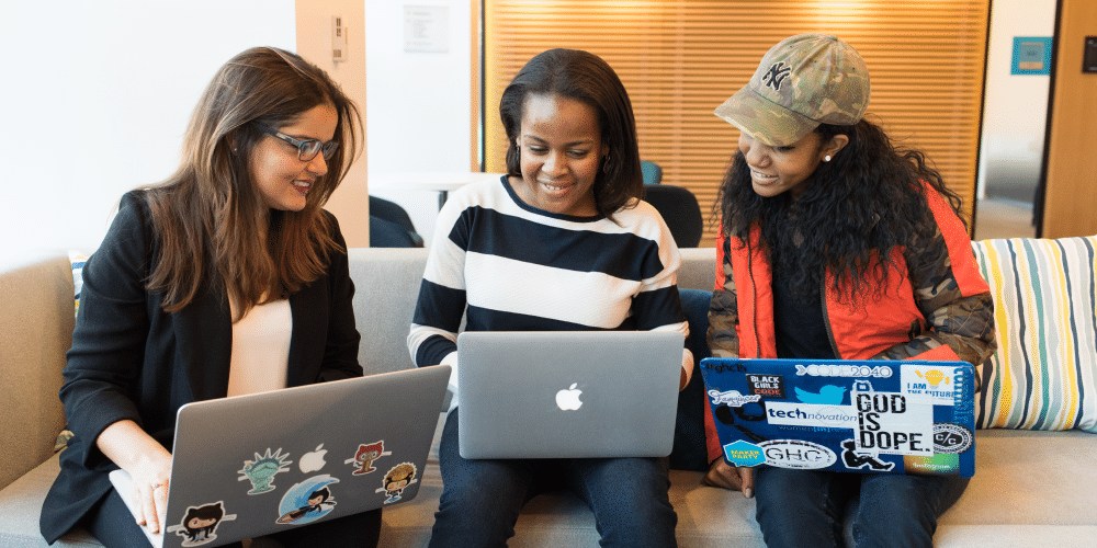 three women gathered on a couch with their laptops in hand