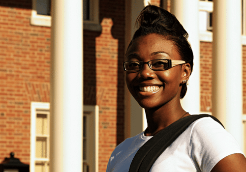 young Black woman with glasses in front of a brick building with columns